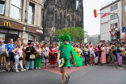 Cologne, Germany - July 9,2023: The christopher street day parade in Cologne, senior man wering green costume and hand fan ith rainbow colors, Cologne cathedral in background
