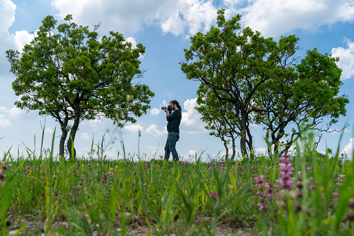 nature photographer taking pictures in the countryside in spring. Taken from the bottom angle.Photographer was seen shooting between two trees. Shot with a full-frame camera in daylight.