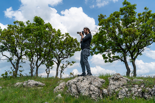 nature photographer taking pictures in the countryside in spring. Taken from the bottom angle.Photographer was seen shooting between two trees. Shot with a full-frame camera in daylight.