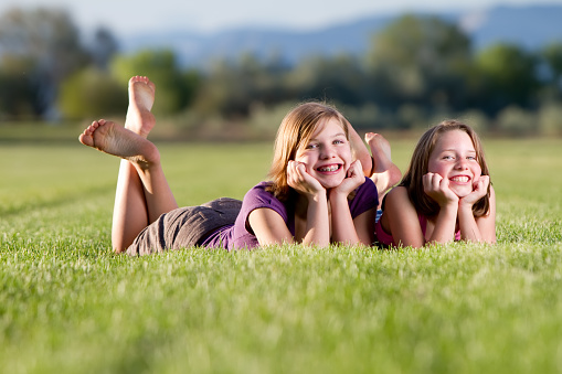 Sisters lying down chin in hands smiling at the camera barefoot.
