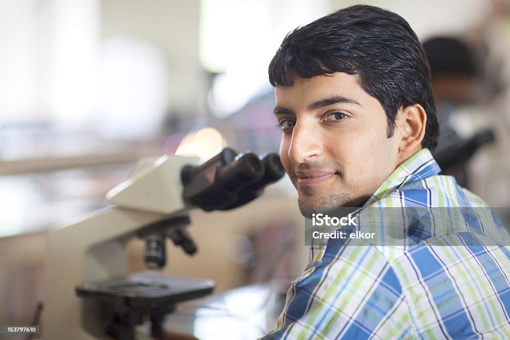 Felice studente indiano con microscopio In un laboratorio - Foto stock royalty-free di India