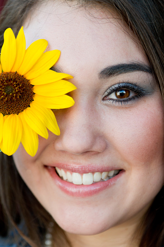 Pretty Asian girl with a yellow sunflower placed over her right eye