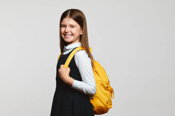 istock Cheerful school kid in uniform smiling for camera and carrying yellow backpack before school studies 1537992321
