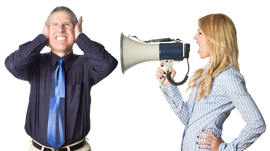 Pretty woman yelling into a megaphone toward a frustrated man with his hands on his ears, isolated on white.  This is a composite shot, not native aspect ratio to camera.