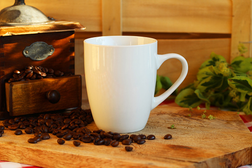 Blank white coffee mug on wooden background with coffee beans and vintage coffee grinder