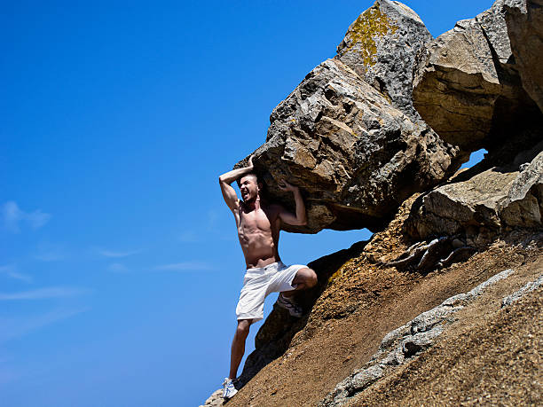 A modern day version of Sisyphus Young man trying to roll a big rock up a hill. sisyphus stock pictures, royalty-free photos & images