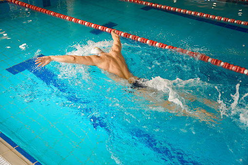 Adult man in white cap engaged in exercises in water, swimming in style of butterfly