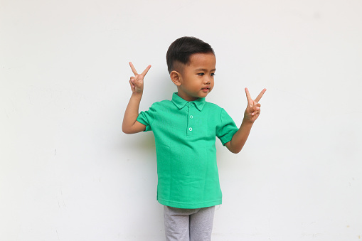 A smiling toddler boy raised hand to show two finger sign, isolated on white background