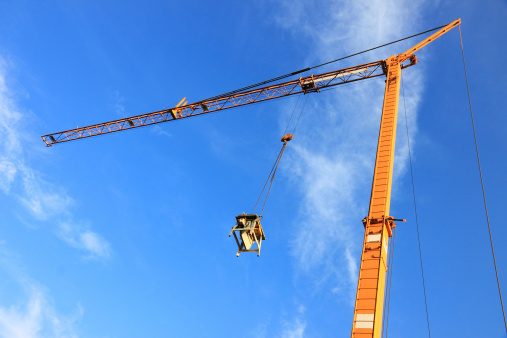 Yellow tower crane on a construction site on a sunny day with deep blue sky in the background. The construction workers already finished their work for the day, this is why the saw is pulled up by the crane.