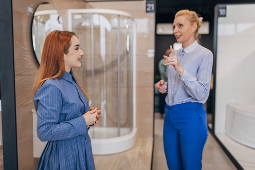 Two women, saleswoman talking to a female customer in bathroom showroom.