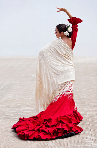Woman traditional Spanish Flamenco dancer dancing outside in a red dress with a cream colored shawl