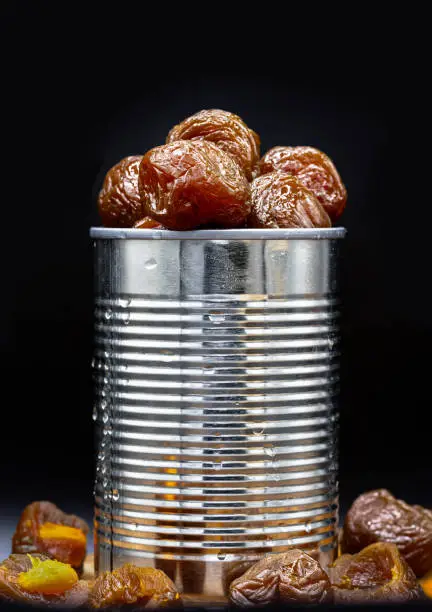 Flavored preserved chinese plums (Preserved fruits) in tin can on dark background. Its flavour has sour, salty and sweet taste. Space for text, Selective Focus.