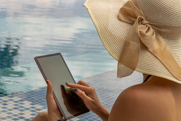 istock Young woman in black bikini using tablet while sitting by the pool in morning time. 1538326357