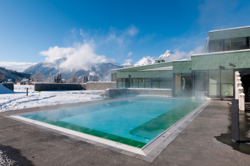 outdoor pool which is steaming  at a cold and clear winter day and mountains in the background