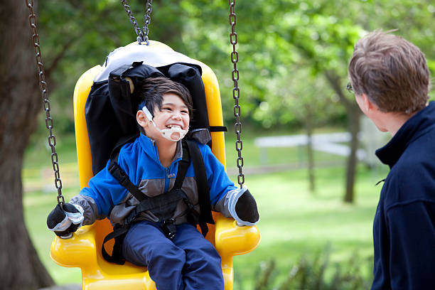 Father pushing disabled son  on yellow handicap swing