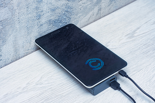 Tablet charging with power bank on a gray wooden table. Portable charger for charging devices