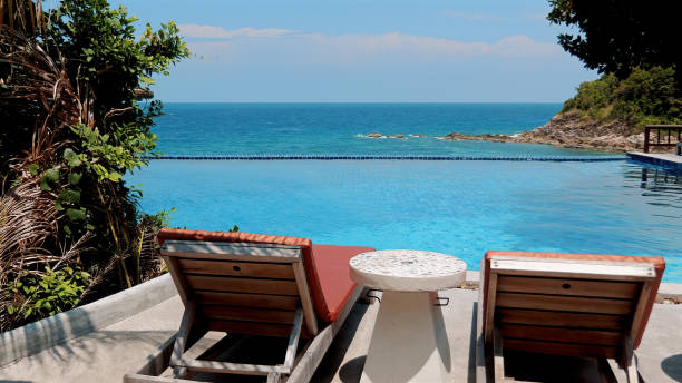 istock Beach chairs and a table beside a sparkling pool with sea view. 1538413318
