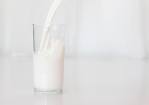 Milk poured into white glass on white background , can be used in the design Campaign for drinking milk for good health