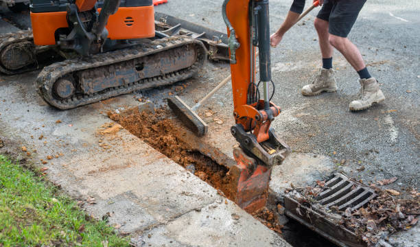 istock Excavator digging up dirt between cut concrete pavement. Man sweeping dirt with broom. Roadworks in Auckland. 1538617799