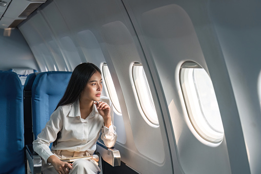 Asian woman passenger sitting in airplane near window and looking out the window.