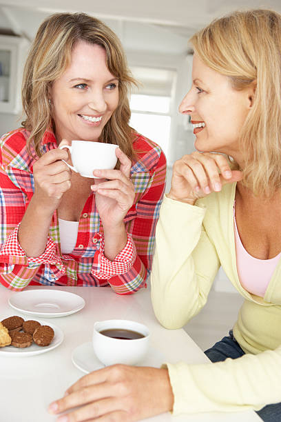 mujeres de mediana edad conversar mientras bebe un café en su casa - coffee buzz fotografías e imágenes de stock