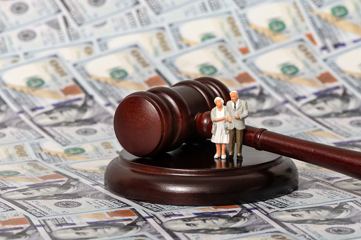 The gavel of the judge and an elderly couple on the background of banknotes in denominations of 100 US dollars