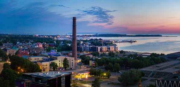 Tallinn Kalamaja District and Baltic Sea in Estonia during Midsummer Sunrise. Colorful Twilight with illuminated Harbour and  Buildingsin the Kalamaja District of Tallinn. Aerial Cityscape Drone View, Stitched Mavic 3 Pro Drone Sunrise Twilight Panorama. Tallinn, Kalamaja, Estonia, Northern Europe, Baltic Countries