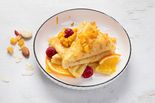 Traditional French crepe Suzette with orange sauce in a white plate on a white background. Top view.