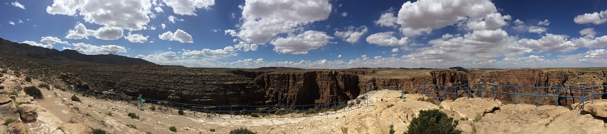A panoramic shot of an impressive canyon with a vibrant blue sky filled with clouds in the background