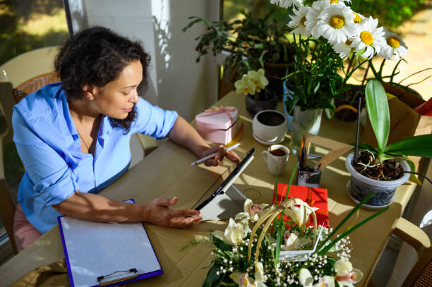 istock Beautiful multi-ethnic woman florist using a digital tablet, sketching, working on floral arrangement in flower shop 1538876347