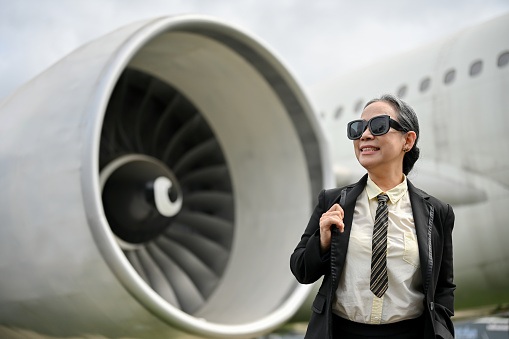 A happy and confident mature Asian businesswoman in sunglasses and a formal business suit boards a plane for her business trip. Transportation concept