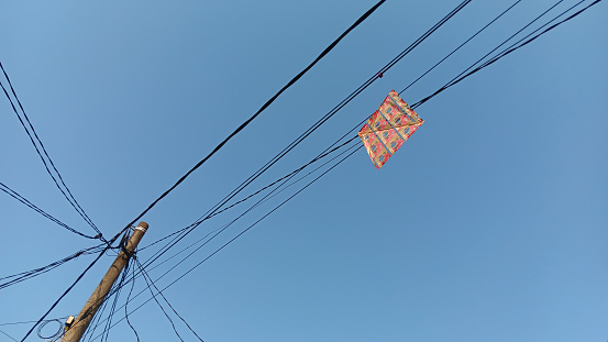 A toy kite stuck in an electric wire against a bright blue sky as a background