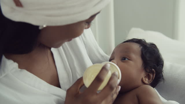 Cherishing Motherhood: African American Mom Nurturing Her Infant with a Milk Bottle | Joyful Bonding at Home