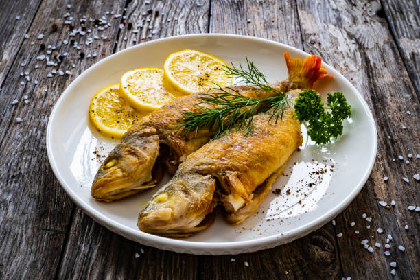 생선 요리 - 나무 테이블에 레몬을 곁들인 튀긴 농어 - trout prepared fish whole grilled 뉴스 사진 이미지