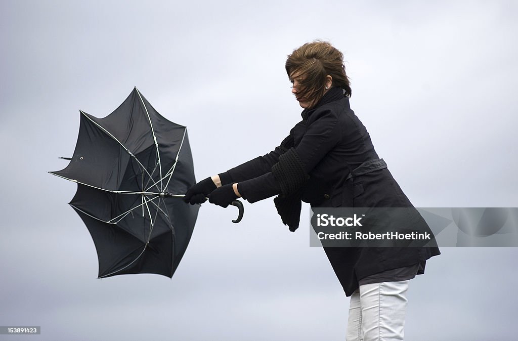 Fighting against the wind A young woman is fighting against the storm with her umbrella Storm Stock Photo