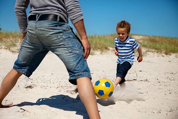 pai e filho a desfrutar de jogo de futebol - beach football imagens e fotografias de stock