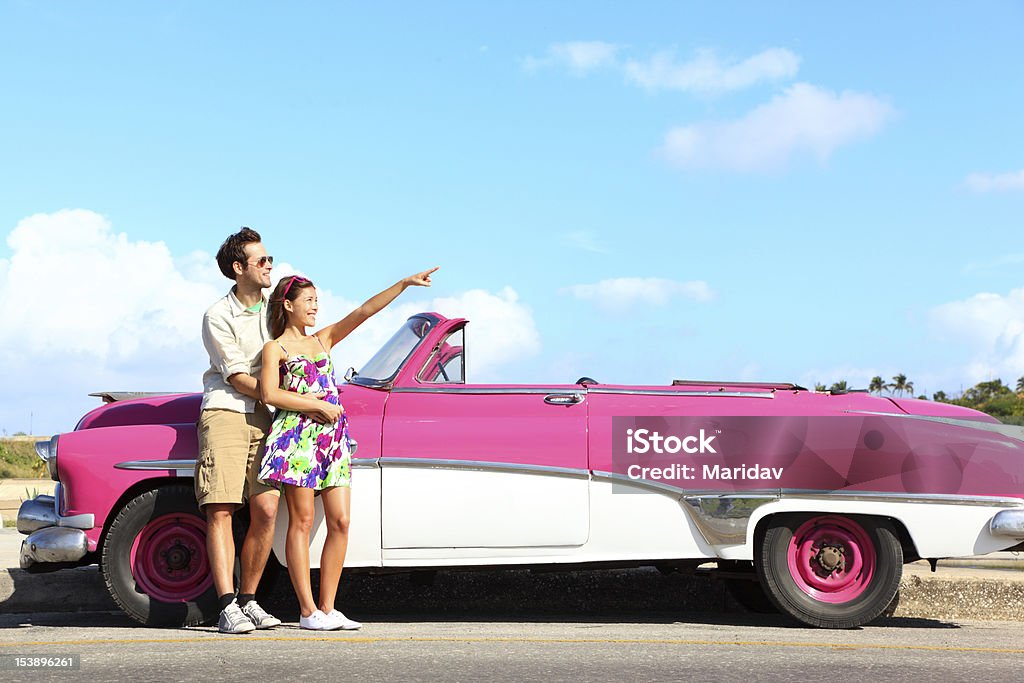 Vintage car - couple pointing Vintage car. Couple pointing looking standing by pink retro vintage car smiling happy. Young couple on summer road trip car holiday in Havana, Cuba. Asian woman, Caucasian man. Convertible Stock Photo