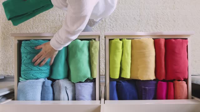 The concept of storage and organization of space. A woman takes a T-shirt from a drawer. Top view.