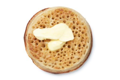 Melting butter on a single crumpet isolated on white.