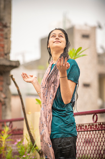 Portrait of happy, cheerful Asian, Indian young woman enjoying the monsoon rain at the rooftop.