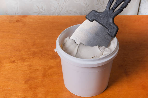 istock White putty in a plastic box ready to repair the old wall. Construction mastic and a spatula are on the table 1539051698
