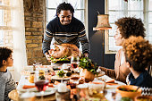 Happy black father bringing Thanksgiving turkey to the table.