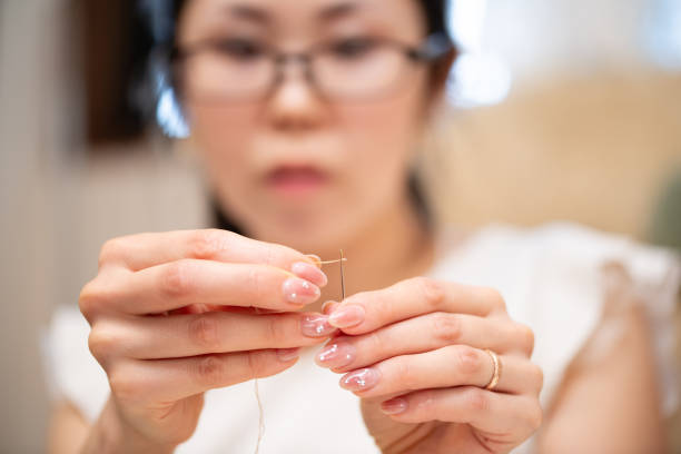 A woman wearing glasses threading a needle