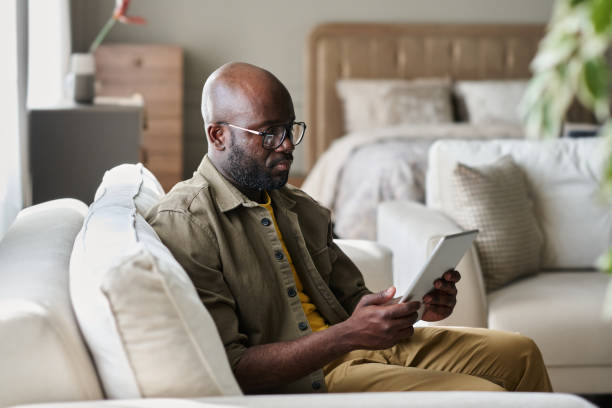 istock Young serious businessman looking at screen of tablet while sitting on couch 1539086030