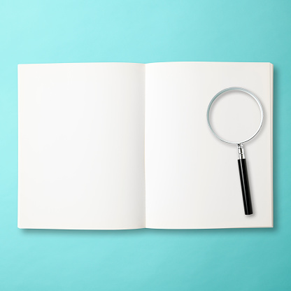 Overhead shot of examining an open blank book with a magnifying glass on light blue background, with clipping path.