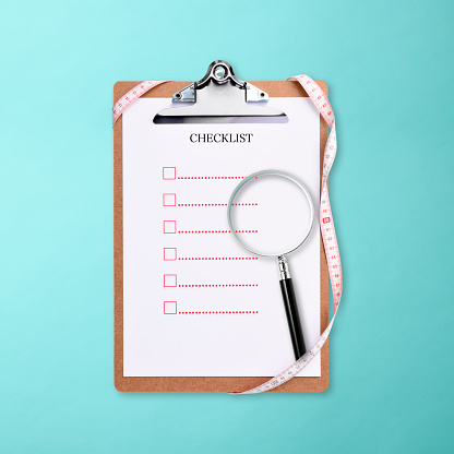 Clipboard with blank Checklist and measurement tape and magnifying glass on light blue background, with clipping path.
Dieting concept