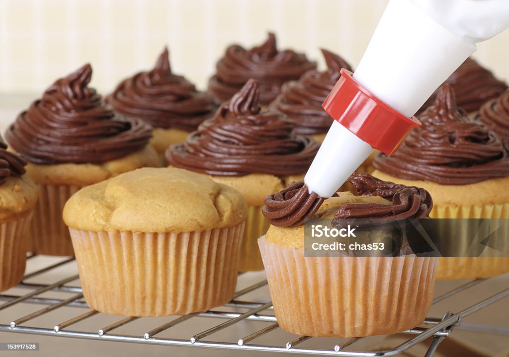 Icing Cup Cakes Piping chocolate frosting onto cup cakes on a wire rack Cake Stock Photo