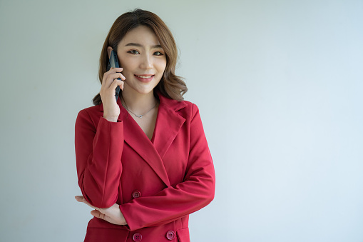 Pretty lovely manager lady successful business Asian women in red suit over white background. Holding and using a mobile smartphone or cellphone.