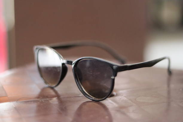 istock A Black sunglass placed on a wooden surface projecting it's reflection on the surface and bright light shining on it in a blurred background 1539194786