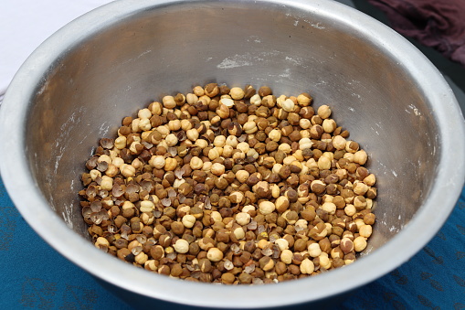 A steel bowl with a pile of roasted chickpeas placed on a blue carpet